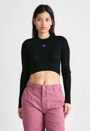 Svart ribbet kort topp med lange ermer og rund halsåpning. Har en liten blå logo på brystet. Sammen med rosa bukser.