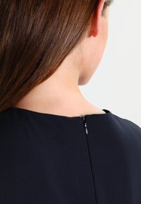 Marintröja med rund halsringning, dragkedja baktill och slät tygstruktur som framhäver en minimalistisk design.