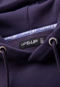 Hoodie marine en tissus doux, avec un label noir notant "LEVEL UP" et des cordons de serrage en lacet avec des embouts en métal.