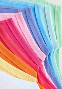 Stos złożonych kawałków bawełnianej tkaniny w kolorach gradientowych od białego, żółtego, pomarańczowego, czerwieni, różu, fioletu, niebieskiego do zielonego, ułożony ukośnie.