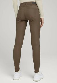 Leggings marrones de ajuste slim, confeccionados en una tela elástica. Presenta dos bolsillos traseros y una cinturilla con un acento azul.