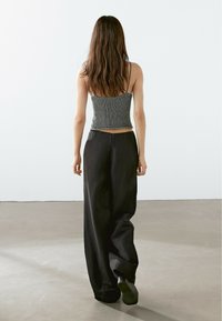 Grå texturerad crop top med tunna band, kombinerad med löst sittande svarta byxor, sedd från baksidan, med en minimal bakgrund.