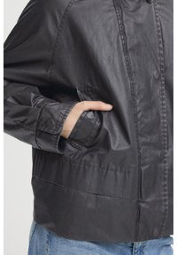 Schwarze, leichte Jacke mit glatter Textur, ausgestattet mit einem Knopfverschluss, seitlichen Taschen und einem lockeren Schnitt.