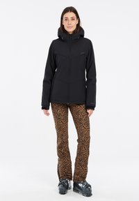 Schwarze isolierte Jacke mit Kapuze, kombiniert mit engen Leopardenmuster-Hosen. Die Jacke hat einen Frontreißverschluss und Reißverschlusstaschen.