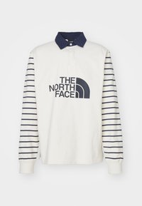 Bílá košile s dlouhým rukávem, modré pruhované rukávy, límec a logo "THE NORTH FACE" na přední straně. Tkanina se jeví jako hladká a ležérní.