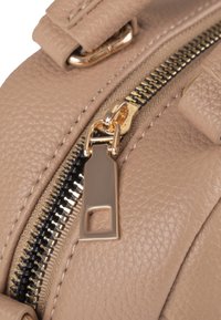 Gros plan sur un tirette de fermeture éclair en or sur un matériau en cuir beige texturé d'un sac avec des accents en matériel doré.