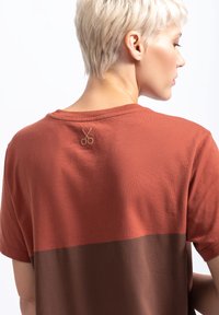 Roodbruine T-shirt met korte mouwen met een donkerbruine horizontale streep, met een geborduurd schaar-embleem aan de achterkant van de hals.