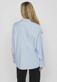 Camisa de gran tamaño en azul claro con mangas largas, yugo trasero y puños con botones, fabricada en una tela suave. Silueta simple y relajada.