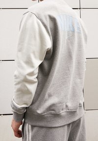 Grå sweatshirt med krämfärgade ärmar, med ljusblå "NIKE"-logotyp och slät textur. Ribbad mudd och midja, avslappnad design.
