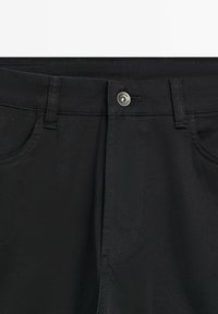 Zwarte broek met een ritssluiting en knoopsluiting, twee zijzakken en een gladde, duurzame textuur. Strakke stikseldetails overal.