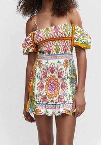 Robe courte, épaules dénudées, présentant un motif floral coloré, réalisée en tissu léger avec un ourlet à volants et des accents audacieux et contrastés.