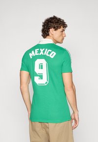 Πράσινο πόλο μπλουζάκι με λευκό γιακά που φέρει τη λέξη «MEXICO» και τον αριθμό «9» σε λευκό, αθλητικός σχεδιασμός με κοντά μανίκια και υφή υφάσματος.