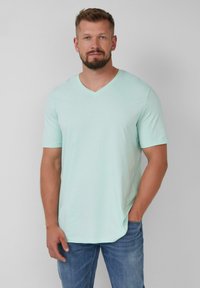 Mintgroene V-hals T-shirt van zachte stof, met korte mouwen en een licht gebogen zoom, gecombineerd met blauwe spijkerbroek.