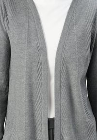 Gray cardigan with vertical ribbing detail, open front, made of knit material. Styled over a white top and black pants. Soft texture.