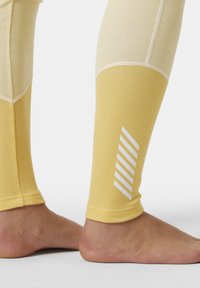 Leggings de color amarillo claro con un acabado texturizado. Presentan un acento de rayas blancas en la parte externa de la pantorrilla. Tejido suave, ajuste ceñido, diseño de longitud hasta el tobillo.