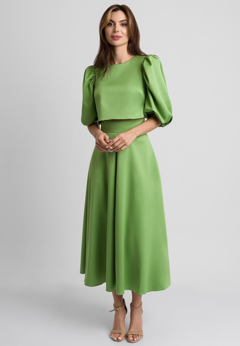 Zielony dwuczęściowy zestaw składający się z krótkiego topu z bufkami oraz długiej spódnicy w kształcie litery A. Gładki materiał o matowym wykończeniu.