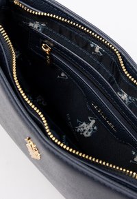 Inredningen av plånboken i marinblått har ett guldzipper och foder med upprepade logotyper, vilket visar rymliga fack för kort och kontanter.