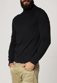 Granatowy sweter z golfem wykonany z miękkiego dzianiny, z długimi rękawami i dopasowanym krojem, w połączeniu z jasnobeżowymi spodniami.