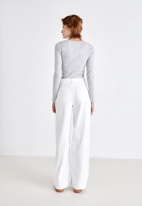 Lichtgrijze lange mouwen crop top, gecombineerd met hoge taille witte wijde broek, met achterzakken en een soepele textuur.