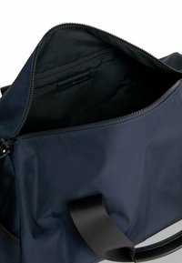 Borsa in nylon blu navy con chiusura a zip. L'interno presenta una tasca con zip separata e una texture liscia. Manico nero per un facile trasporto.