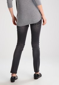 Jeans negros de corte ajustado con un ligero efecto de desgaste, cintura media y dobladillos remangados, combinados con una blusa gris de manga larga y zapatos negros.