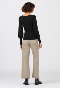 Haut noir ajusté à manches longues bouffantes, associé à un pantalon beige à jambes larges avec ourlet effiloché, porté avec des bottines noires.