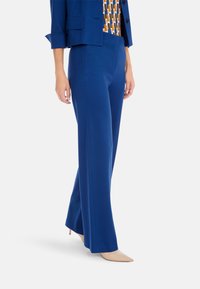 Blue, flared trousers made from smooth fabric; paired with a blue blazer and patterned top. Beige pointed heels complete the outfit.