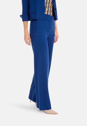 Blue, flared trousers made from smooth fabric; paired with a blue blazer and patterned top. Beige pointed heels complete the outfit.