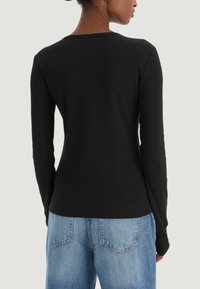 Czarna prążkowana bluzka z długim rękawem i okrągłym dekoltem, dopasowany fason i gładka faktura, zestawiona z jasnoniebieskimi jeansami z wysokim stanem.