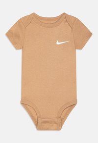 Un body en coton beige à manches courtes et col rond. Caractérisé par un logo Nike blanc sur le haut à gauche de la poitrine. Texture lisse.