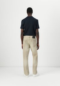 Camiseta de algodón azul marino, combinada con jeans de pierna recta en beige claro que cuentan con una etiqueta en el bolsillo trasero. Textura suave, diseño minimalista.