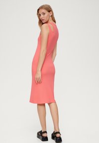 Koronkowa sukienka o dopasowanym kroju, wykonana z dzianiny prążkowanej w kolorze koralowym, bez rękawów, z wycięciem z tyłu oraz długości do kolan. W połączeniu z czarnymi butami na platformie.
