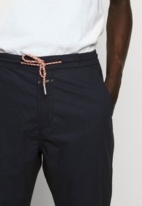 Shorts de bain bleu marine avec taille élastique, dotés d'un cordon de serrage texturé orange et blanc, et de poches latérales pour le rangement.