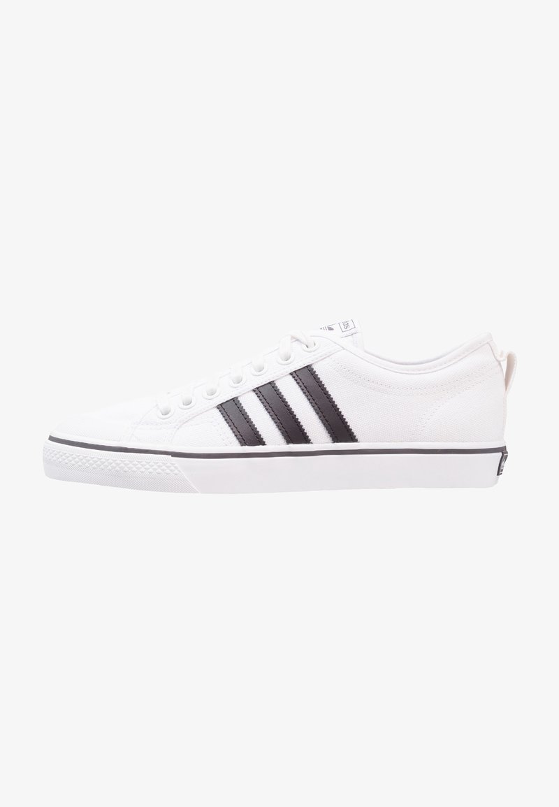 White canvas sneaker with black stripes; rounded toe, flat sole, lace-up front, and a tab at the heel. Textured fabric and sleek design.