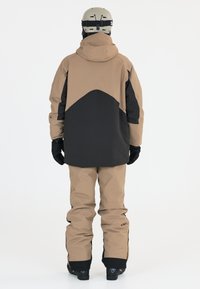 Snöbräda jacka och byxor i beige och svart. Jackan har en huva, kontrasterande färgblockdesign och är ihop med matchande baggybyxor.