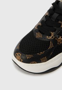 Μαύρα αθλητικά παπούτσια με υφή πλένης και καφέ μοτίβα λογότυπου, μαύρους κορδόνες και λευκή σόλα με διακρι�τική μπλε λεπτομέρεια.