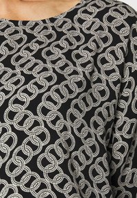 Tecido preto com um padrão de corrente entrelaçada em branco. O design é ousado, com laços suaves e arredondados e detalhes uniformemente espaçados.