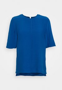 Niebieski top z krótkim rękawem, charakteryzujący się okrągłym dekoltem, gładką strukturą oraz delikatnym detalem szwów z przodu i z tyłu. Dół jest lekko dłuższy z tyłu.