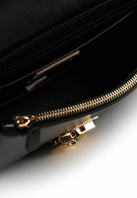 Zwarte leren handtas interieur met gouden rits, voorzien van een gladde textuur en een gouden sluiting met rode accenten.