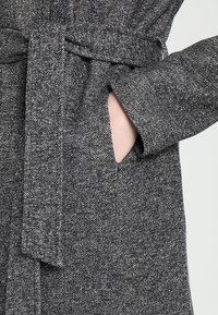 Grijze textuur bathrobe met een tailleband, voorzien van grote zakken. De stof lijkt zacht en warm, met een subtiel patroon.