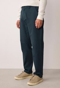 Chino bleu marine en mélange de coton, présentant une coupe droite, un tissu texturé et une taille plate. Associé à des baskets beige.