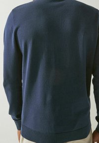 Pull tricoté bleu marine avec un col rond, des manches longues et un ourlet côtelé ajusté. Texture douce avec un léger brillant et un design épuré.