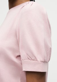 Απαλό ροζ κοντομάνικο πουκάμισο με φουσκωτό μανίκι, φορεμένο από άτομο με μέτριο τόνο δέρματος, κοντινή λήψη στον ώμο και το πάνω μέρος του χεριού.