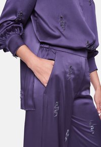 Purple satin outfit featuring a loose top with puffed sleeves and embellished snake patterns, paired with matching pants and side pocket.