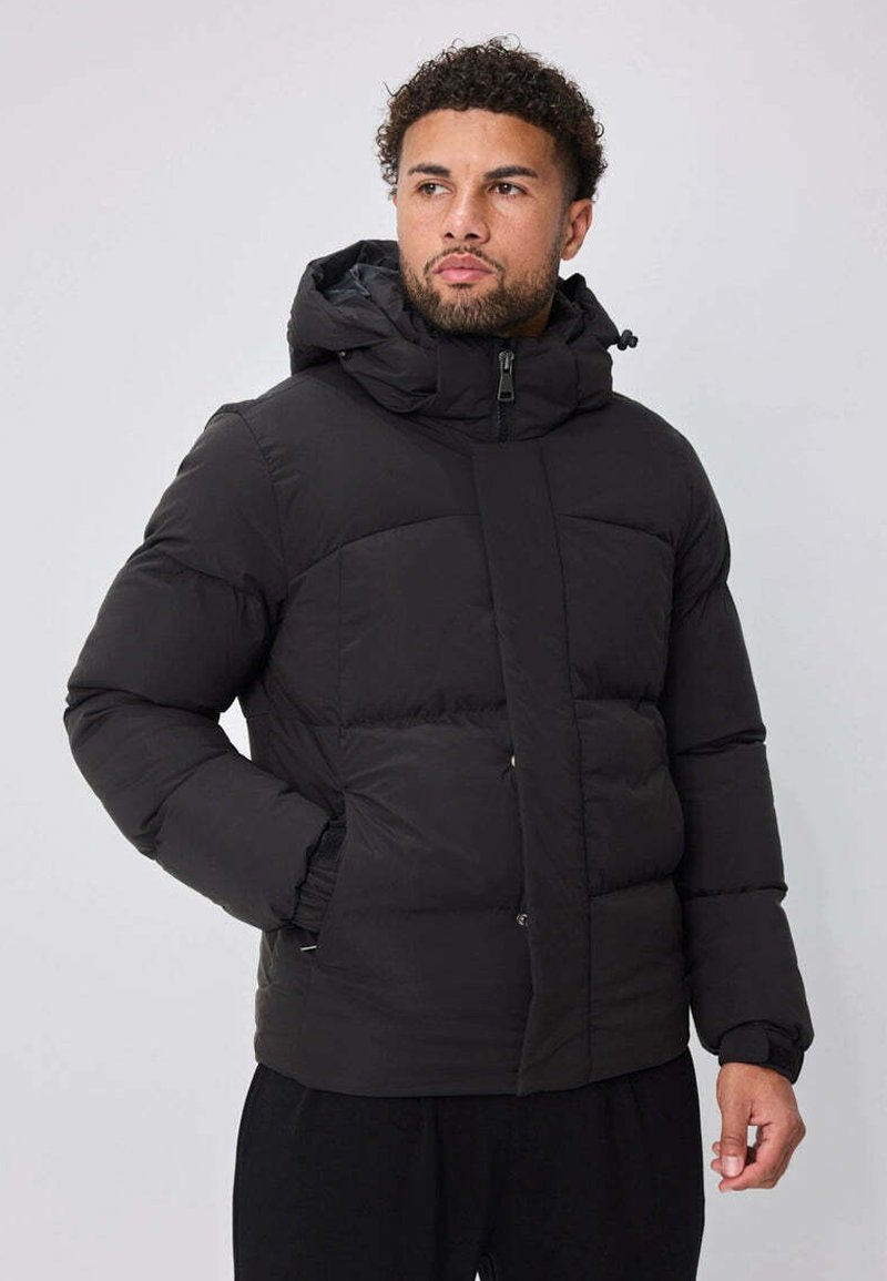 Doudoune noire avec capuche, présentant une fermeture éclair sur le devant, un design matelassé et deux poches latérales. Texture douce avec une finition lisse.