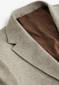 Blazer beige texturizado con solapa y forro marrón suave, que presenta un patrón tejido para un detalle adicional.