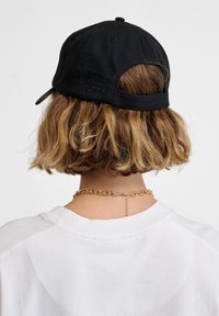 Zwarte honkbalpet met een gebogen rand, gestructureerde stof, verstelbare strap aan de achterkant en een reliëflogo op de achterkant. Witte shirt met een ronde halslijn.