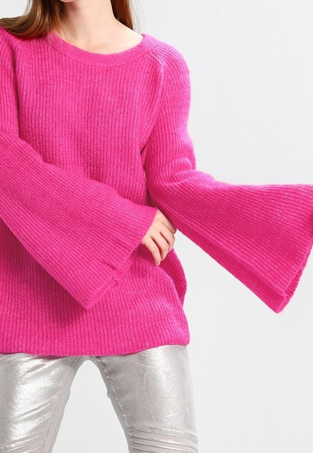 Pull tricot rose vif avec manches larges en forme de cloche. Texture côtelée, encolure arrondie, associé à un pantalon argenté brillant.