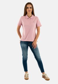 Polo rosa con due bottoni, abbinata a jeans skinny azzurri chiari e sneakers beige con dettagli rossi. Tessuto liscio e vestibilità classica.