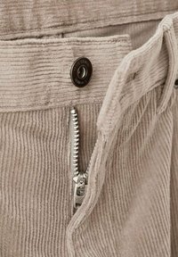 Pantalones de pana beige con un botón de metal y una cremallera plateada, con textura acanalada vertical y costuras reforzadas a lo largo de la cintura.